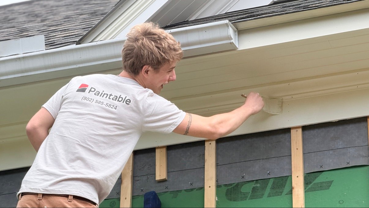 Paintable crew member painting a soffit on a Vermont home